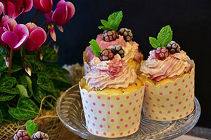 Three cupcakes with decorations in a plate next to flowers